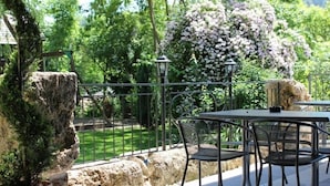 An outdoor patio with a table and chairs, surrounded by rocks and potted plants, with a view of a garden and trees. - Hotel Restaurant L'Acacia (Marly)