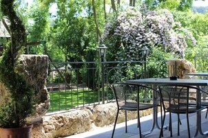 Un patio al aire libre con una mesa y sillas, rodeado de rocas y plantas en macetas, con vista a un jardín y árboles.