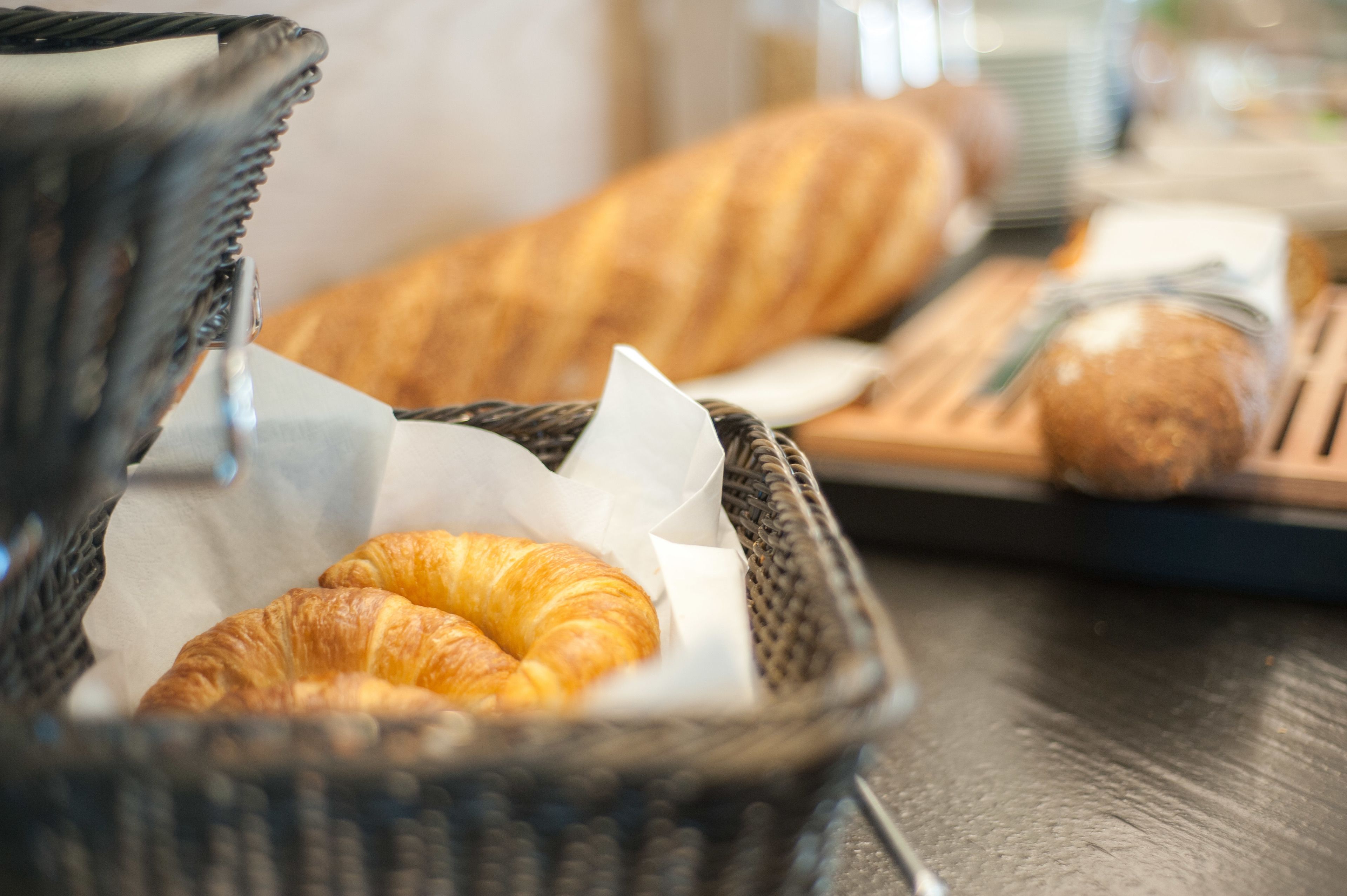 Una cesta con cruasanes y una baguette sobre una mesa.