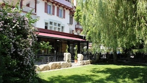 A courtyard with a covered seating area, stone walls, and a large tree. - Hotel Restaurant L'Acacia (Marly)