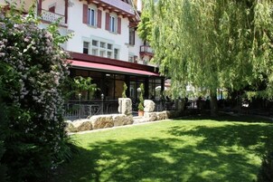 Un patio con zona de estar techada, muros de piedra y un árbol grande.