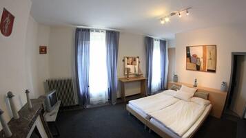 Una habitación de hotel con una cama, un escritorio con computadora, un radiador y cortinas.