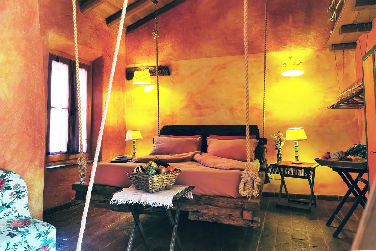 A cozy room with a bed, two bedside tables with lamps, a hanging chair, and a wooden floor.
