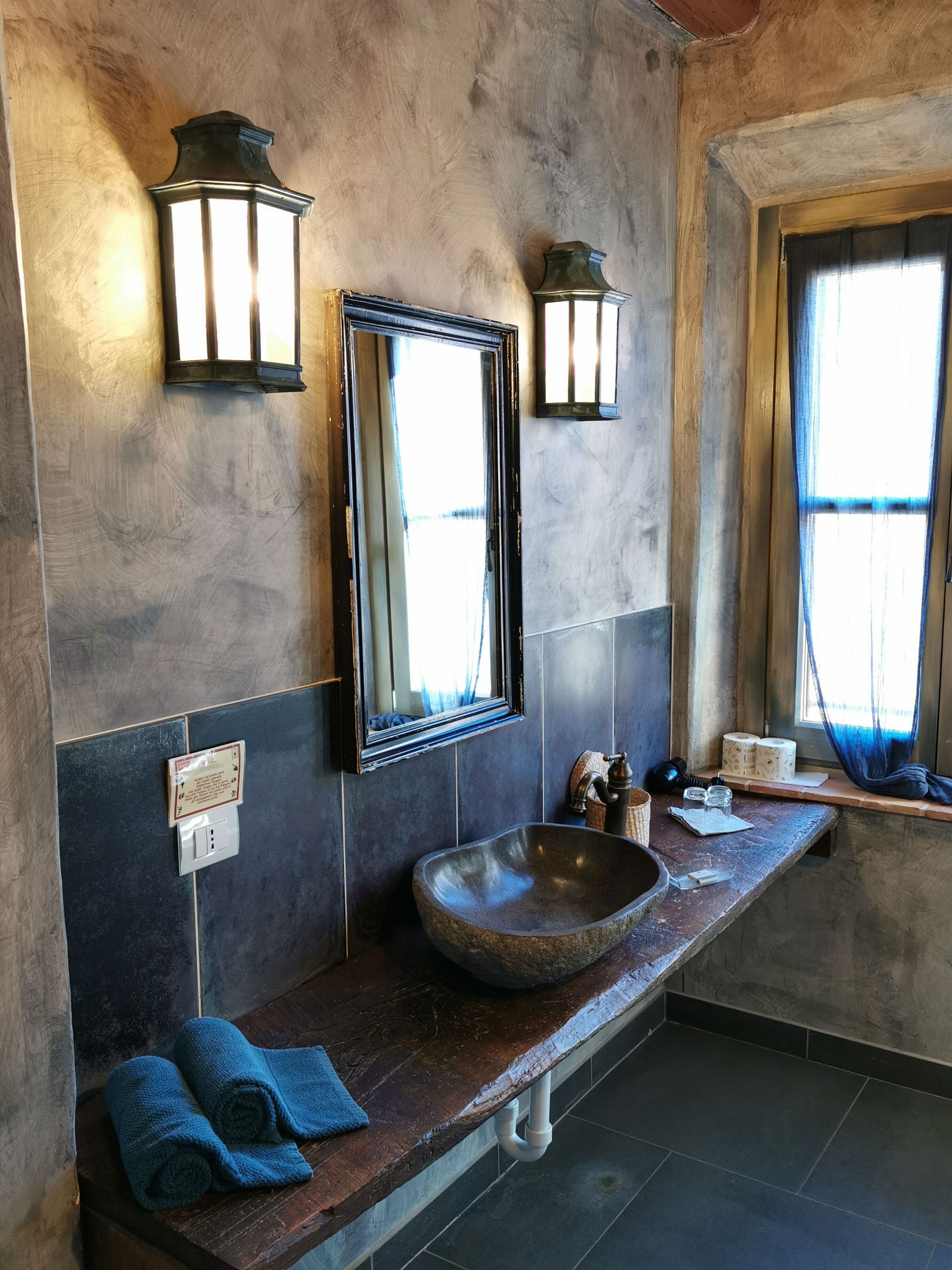 A bathroom with a stone sink, two wall-mounted lights, a mirror, and towels on the counter.
