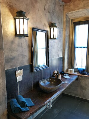 A bathroom with a stone sink, two wall-mounted lights, a mirror, and towels on the counter. - Galbusera Bianca (La Valletta Brianza)