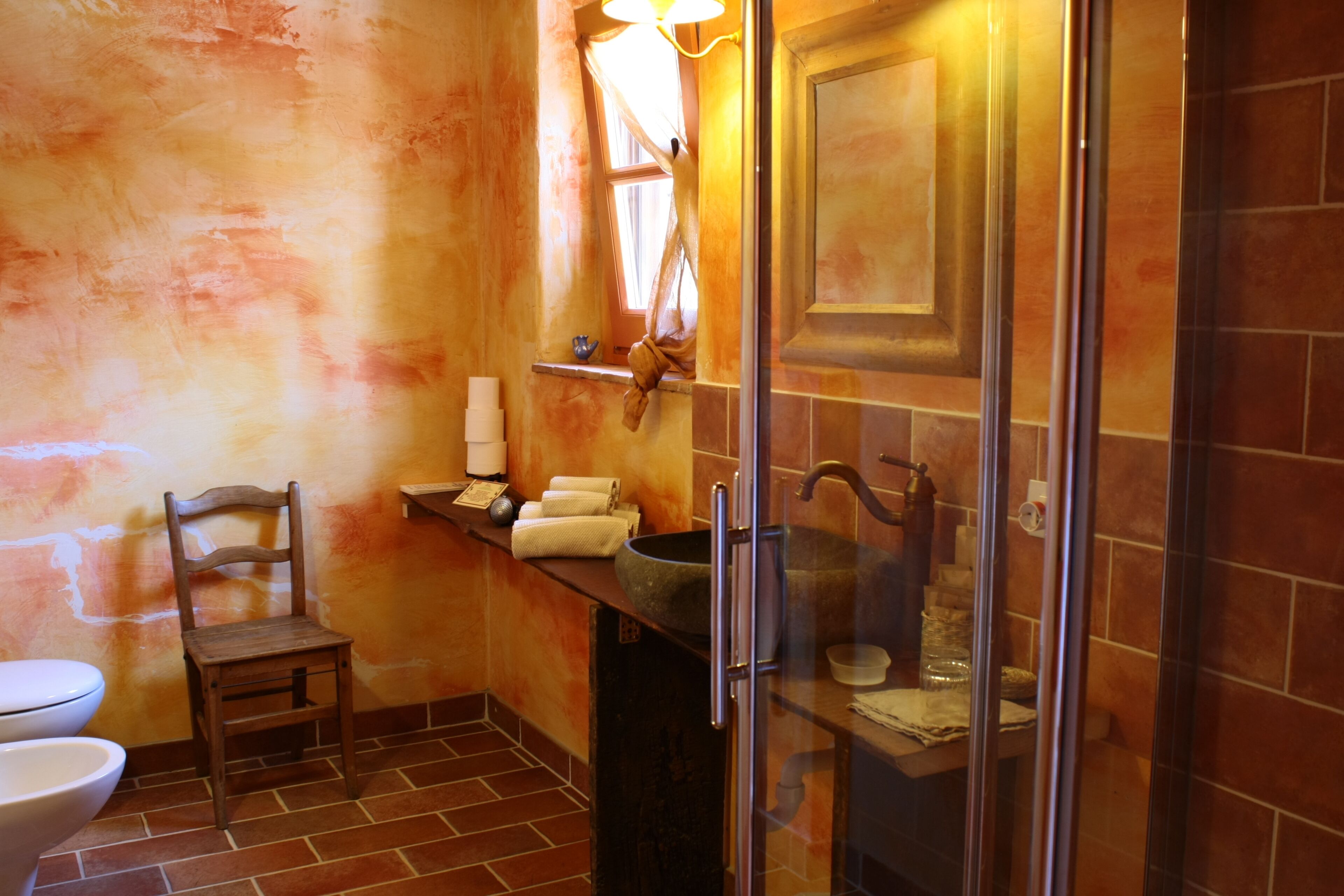 Ein Badezimmer mit einem Holzhocker, einem Waschbecken und einer Duschkabine aus Glas.