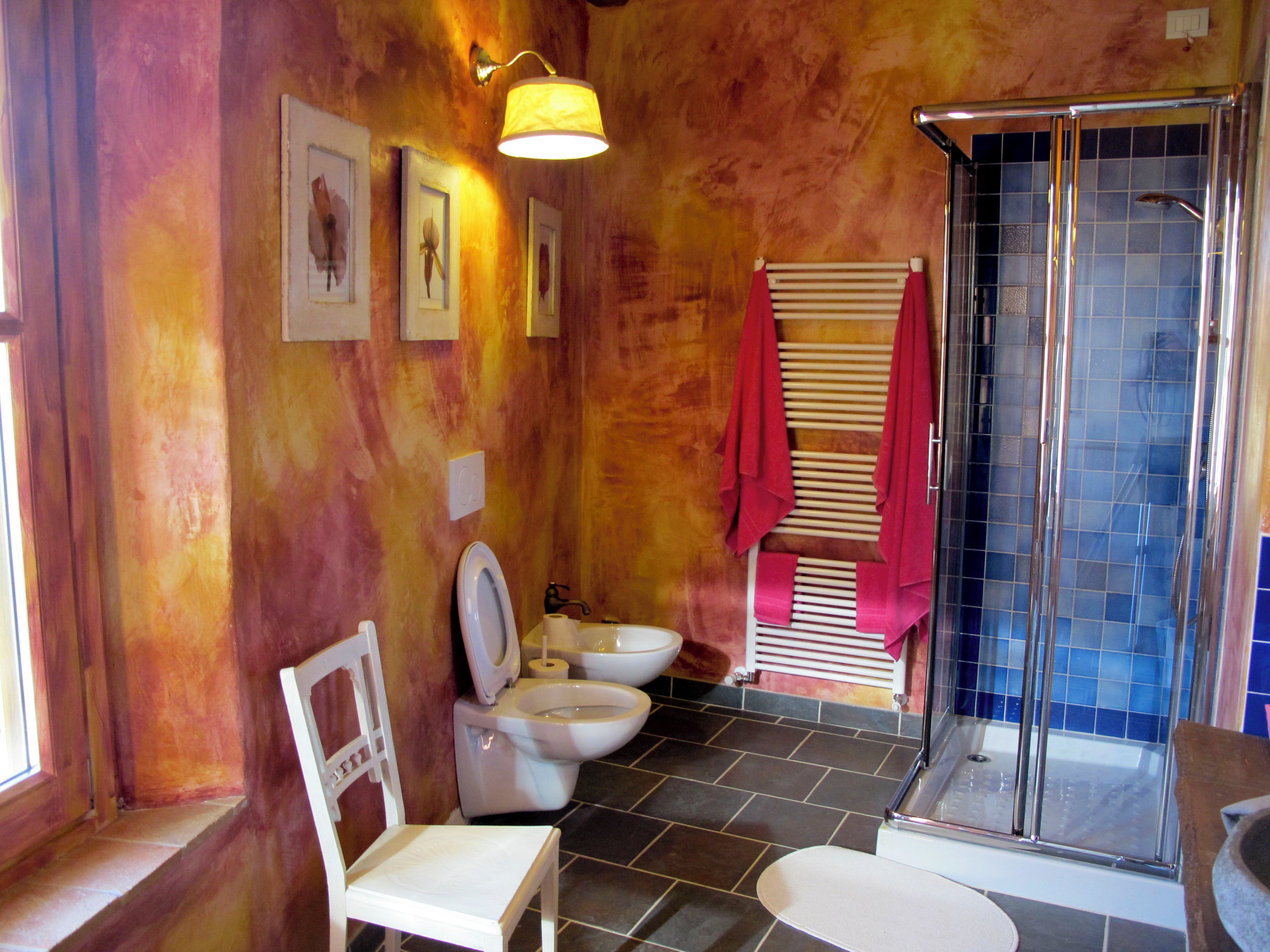 Une salle de bain avec une douche, deux toilettes, un lavabo et une chaise.