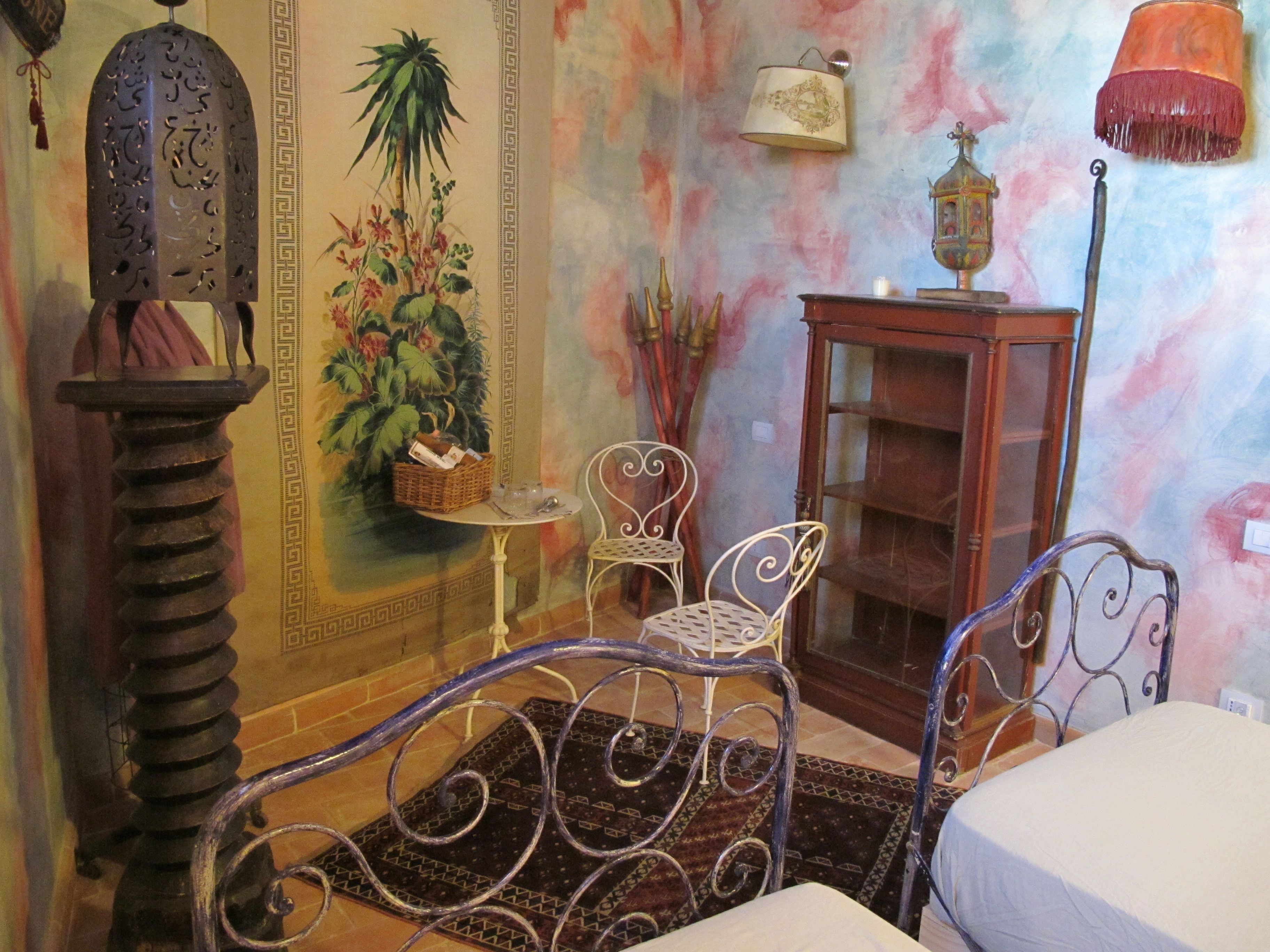 Une pièce comprenant un lit, une chaise en métal, une petite table, une lampe, un mur décoratif et un meuble.