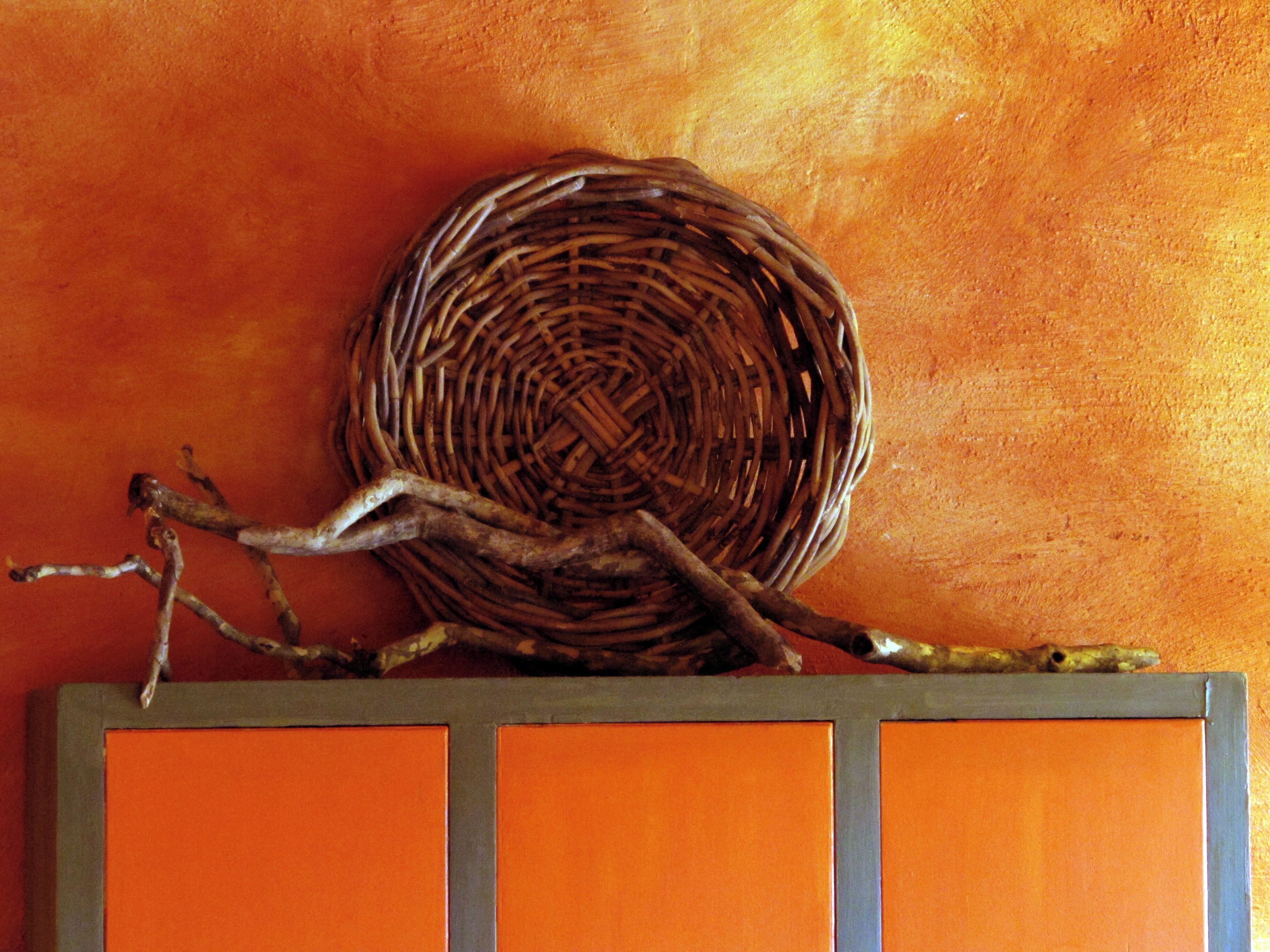 A wicker basket on a wall with branches.