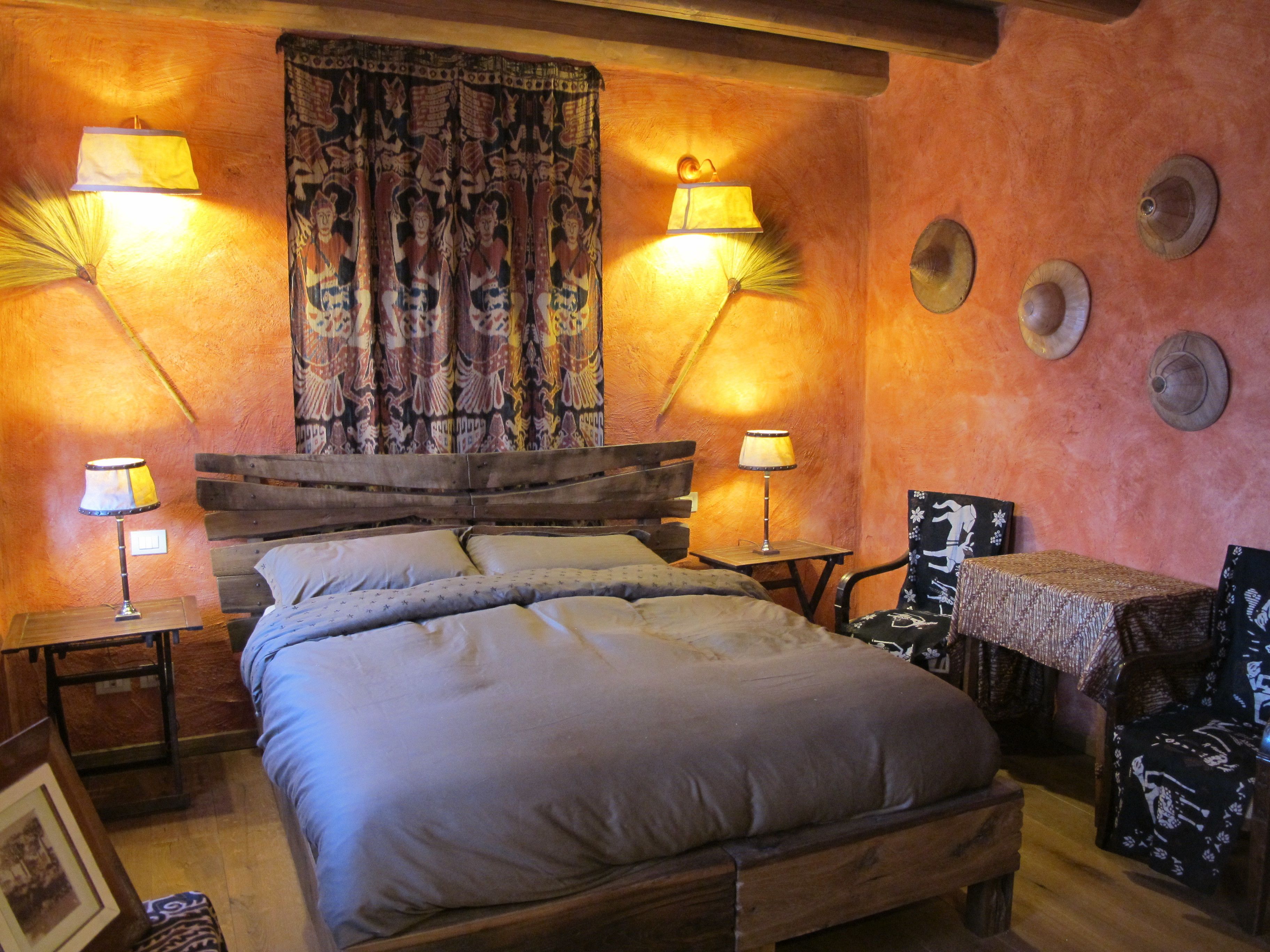 A cozy bedroom with a wooden bed, two bedside lamps, a patterned curtain, and a small table with a chair.