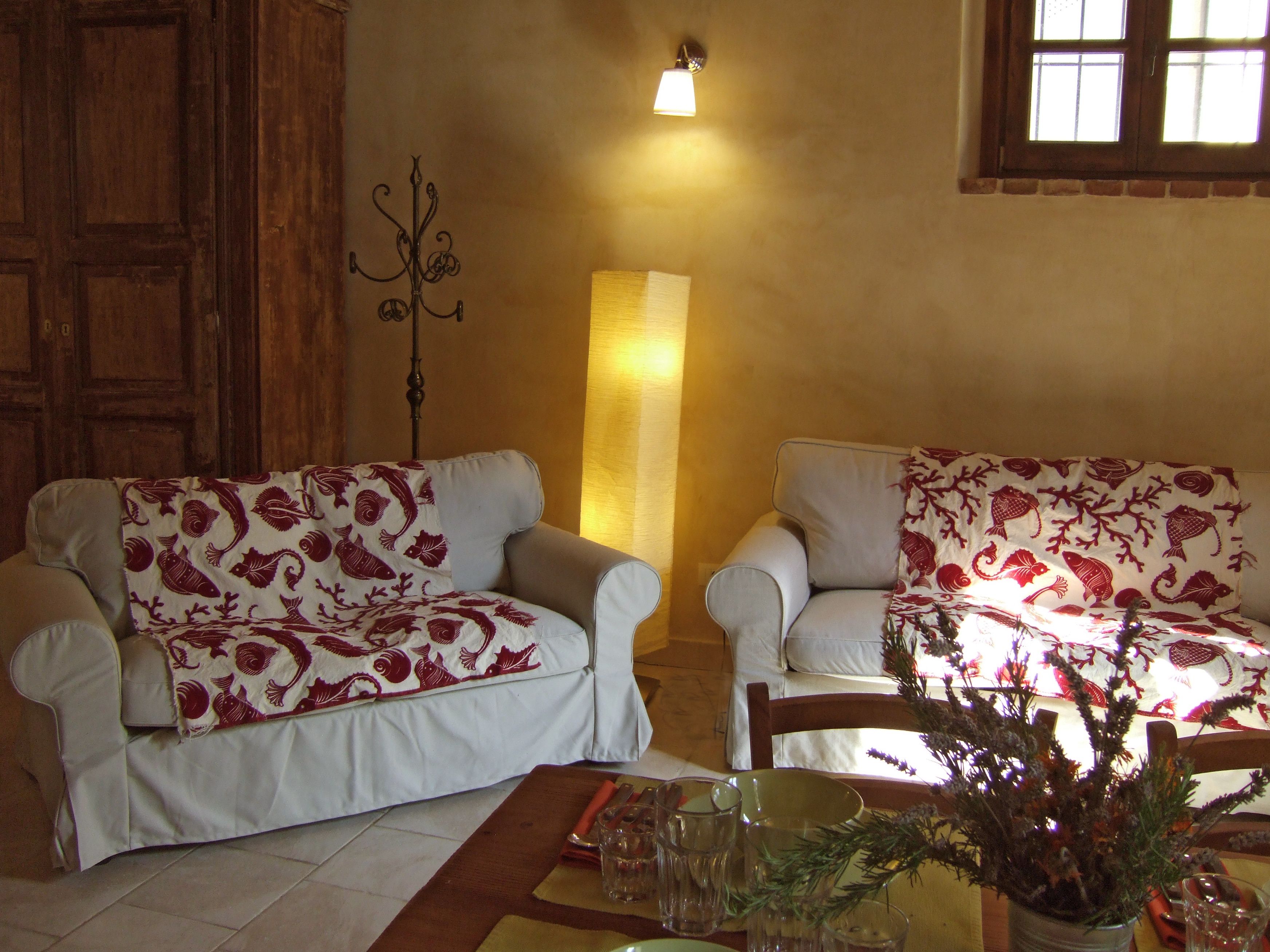 Une pièce avec deux canapés blancs ornés de motifs rouges et blancs, un grand lampadaire et une fenêtre laissant entrer la lumière naturelle.