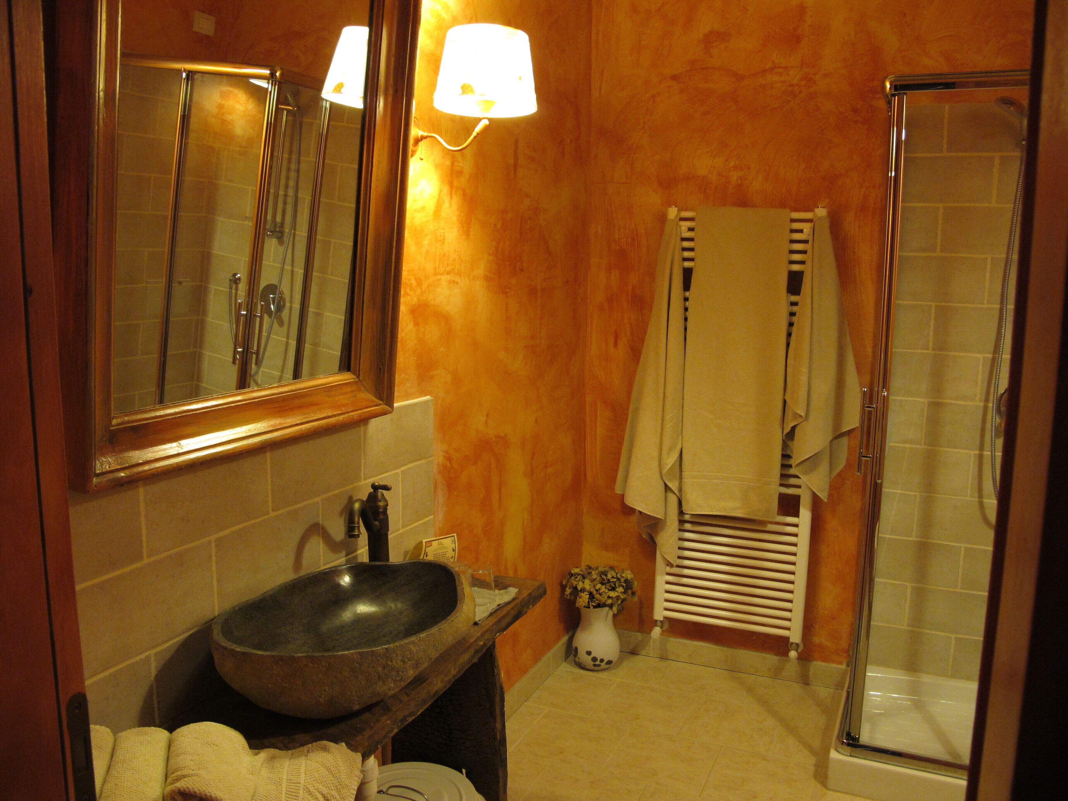 Un baño con un espejo grande, un lavabo, toallero, ducha y una lámpara en la pared.
