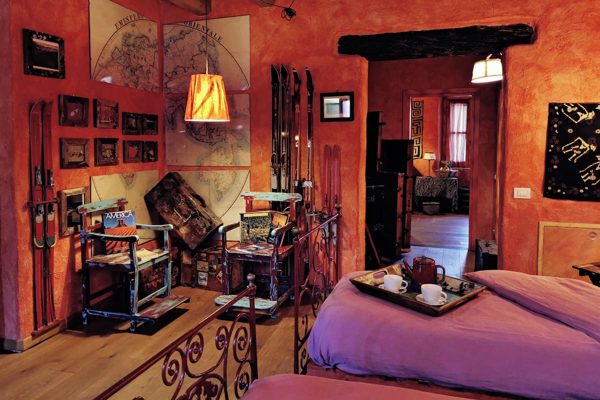 A cozy room with a wooden ceiling, a map on the wall, skis leaning against the wall, and a bed with a purple pillow.