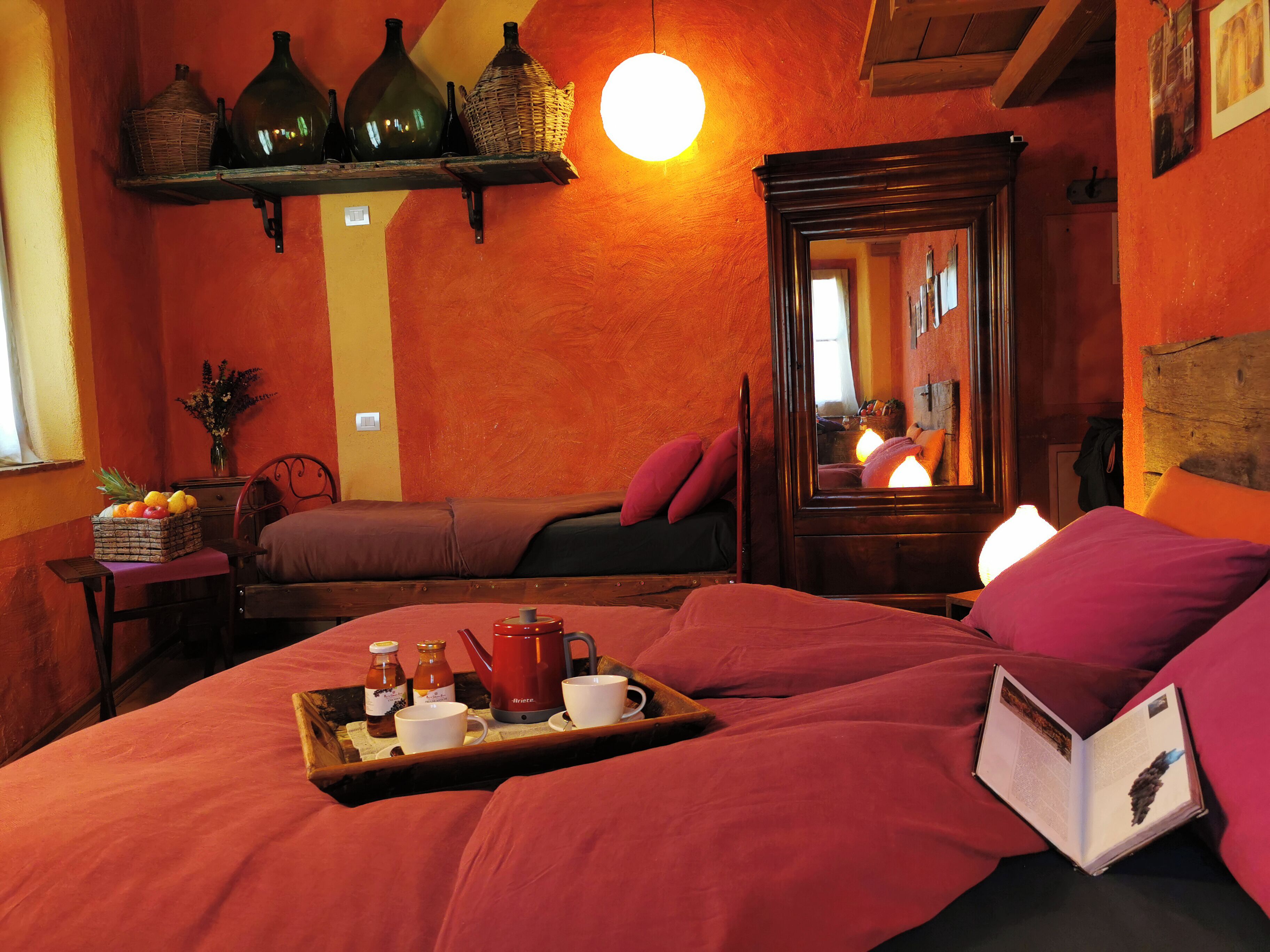 Une chambre confortable avec un lit, une table de chevet sur laquelle se trouve un plateau avec des articles pour le petit-déjeuner, un miroir et une étagère avec des bouteilles et des paniers.