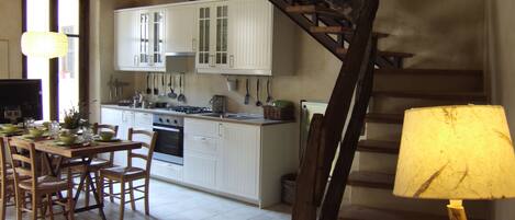 A kitchen with white cabinets, a dining table set with chairs, and a staircase leading to another level.