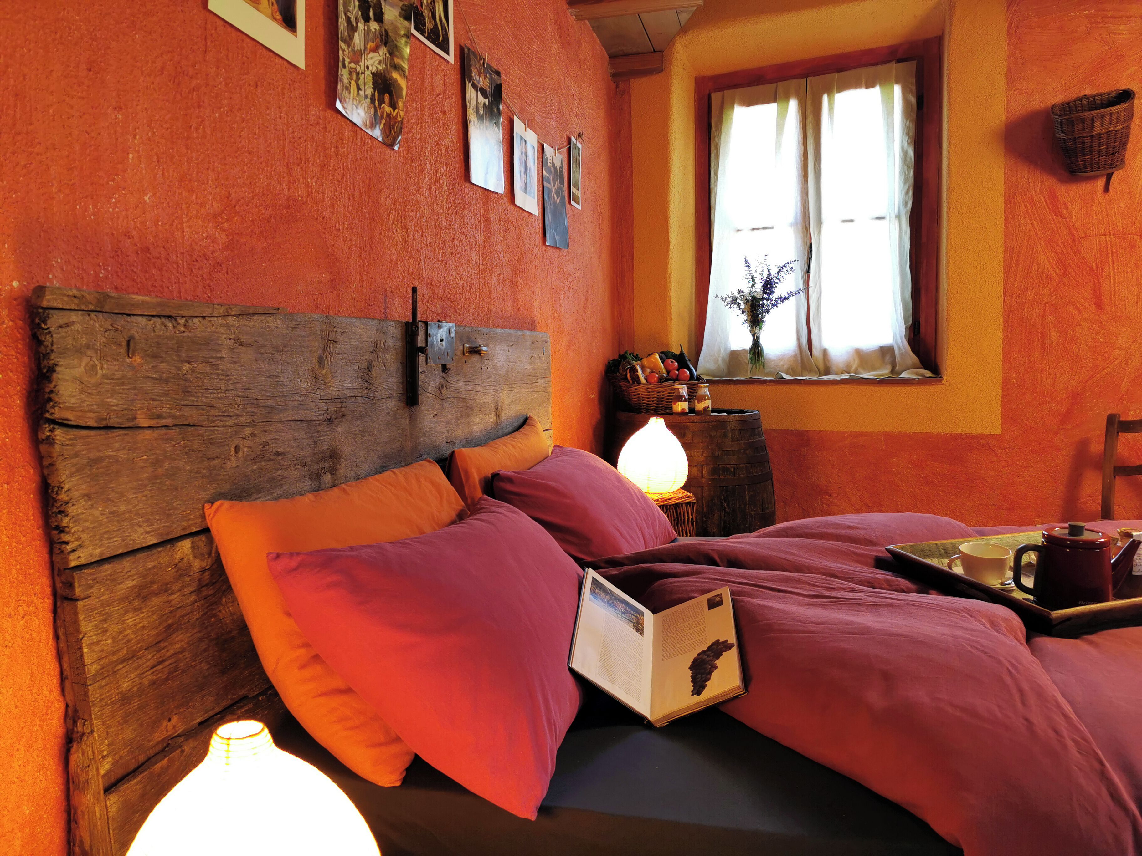 Una habitación acogedora con cabecera de madera, cama con ropa de cama naranja, mesita de noche con lámpara y ventana con cortinas.
