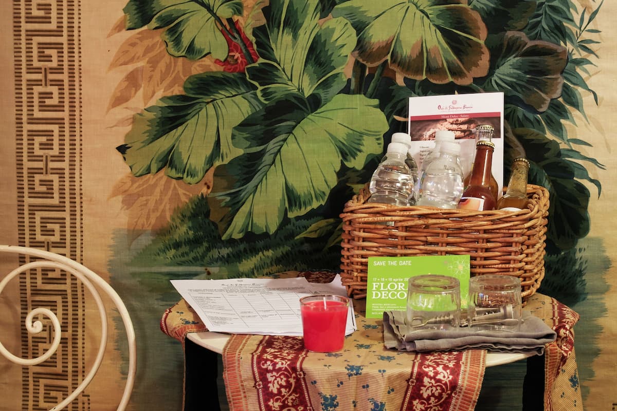 A table with a wicker basket containing bottles, a glass of red drink, a menu, and a green card.