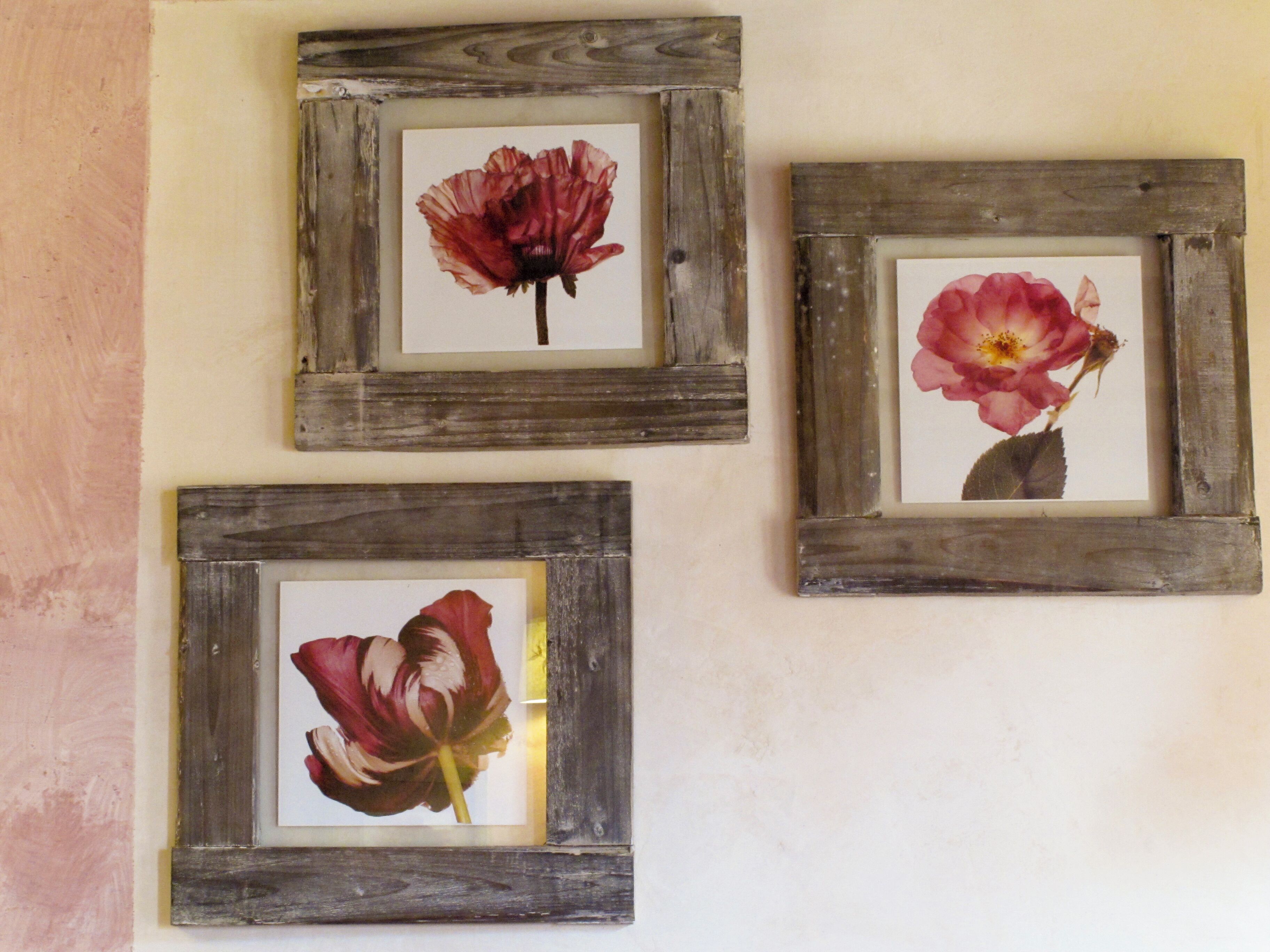 Drie ingelijste foto’s van bloemen aan een muur.