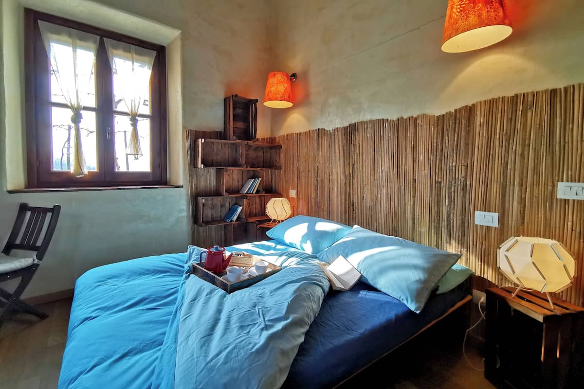 A bedroom with a bed, a window with curtains, a bookshelf, and a wall-mounted lamp.