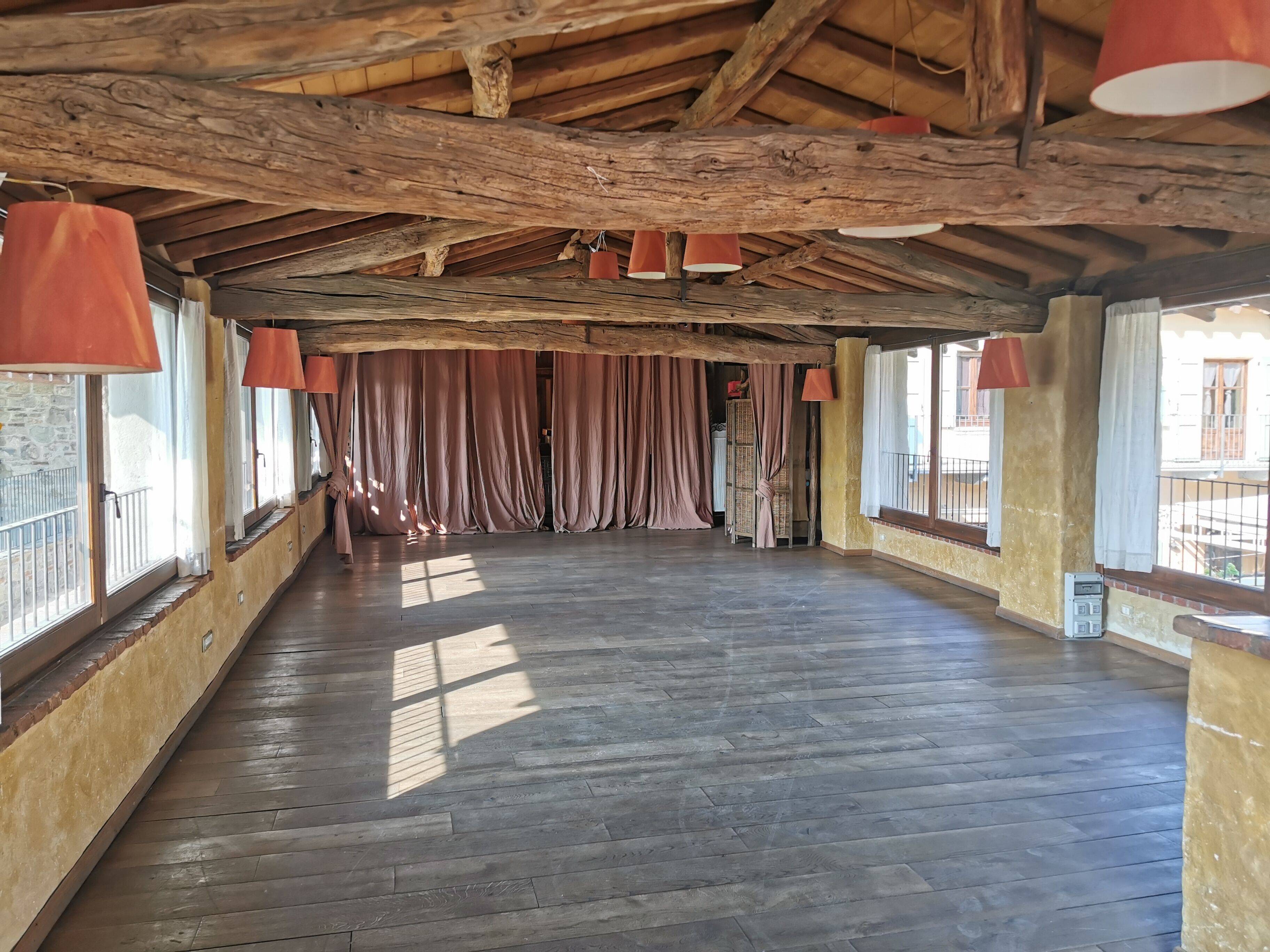 A spacious room with wooden floors, large windows, and red hanging lamps.