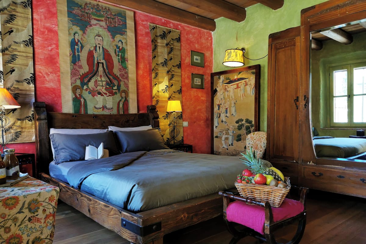 A traditional room with a wooden bed, a chair with a fruit basket, and a mirror.