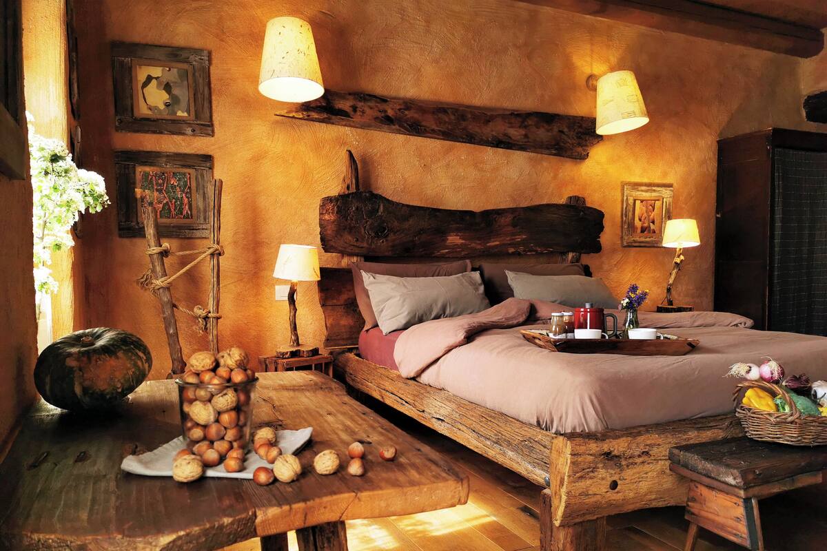 A rustic bedroom with a wooden bed, two bedside tables with lamps, a wooden nightstand, and a wooden bench.