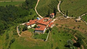 An aerial view of a large estate with terraced vineyards, a central building with a red-tiled roof, and surrounding greenery. - Galbusera Bianca  (La Valletta Brianza)