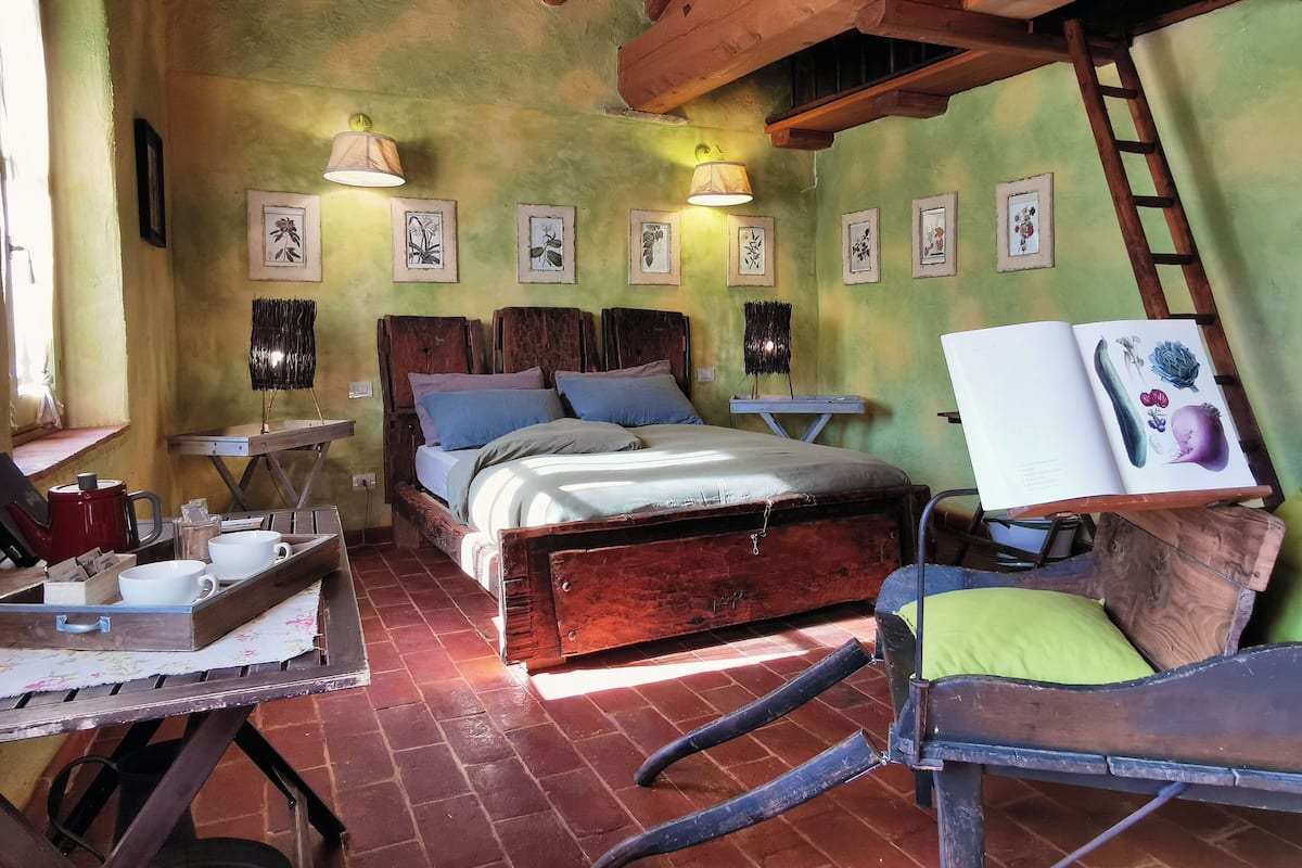 A rustic bedroom with a wooden bed, two bedside tables, a small desk, and a ladder.