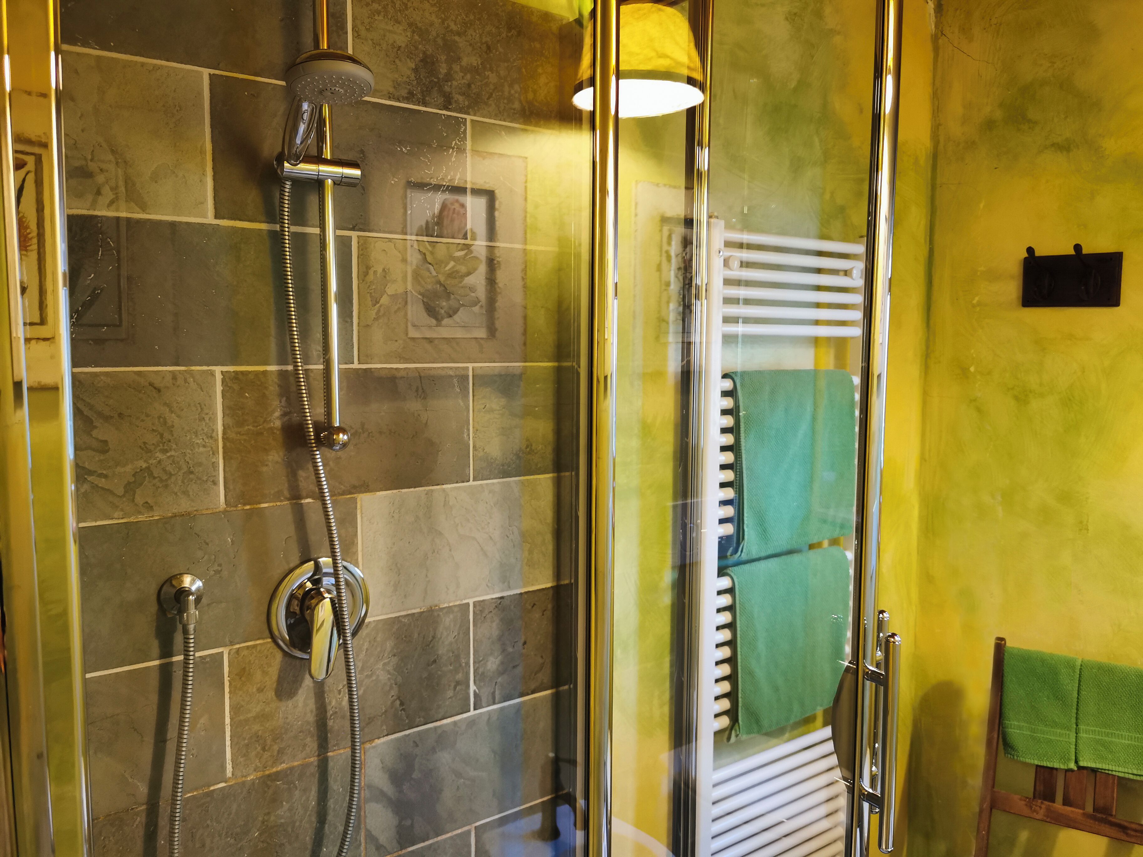 Eine Dusche mit Glastür, ein Handtuchhalter mit einem grünen Handtuch und einer gelben Wand.