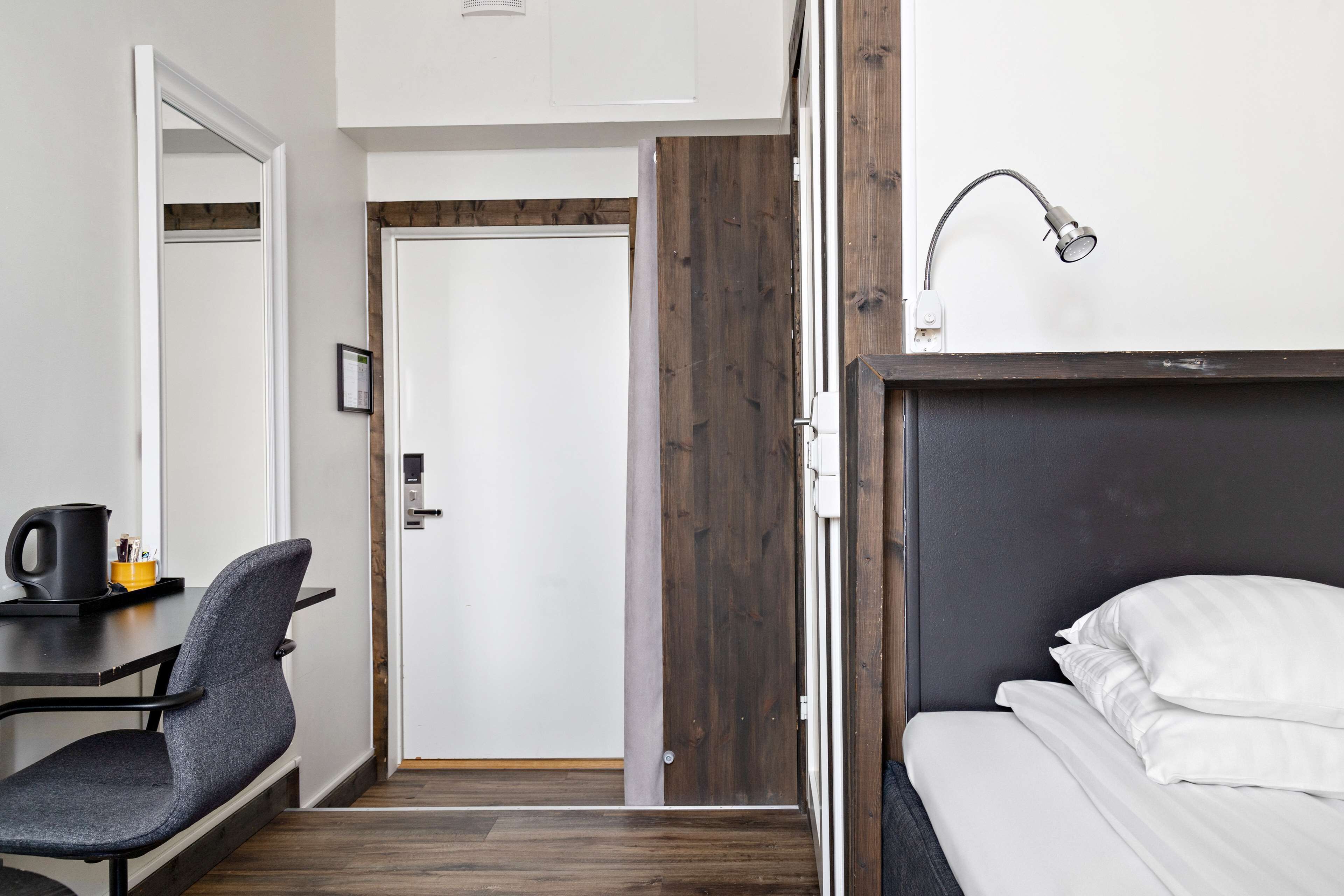 A hotel room with a bed, a desk with a chair, a coffee maker, and a door leading to another room.