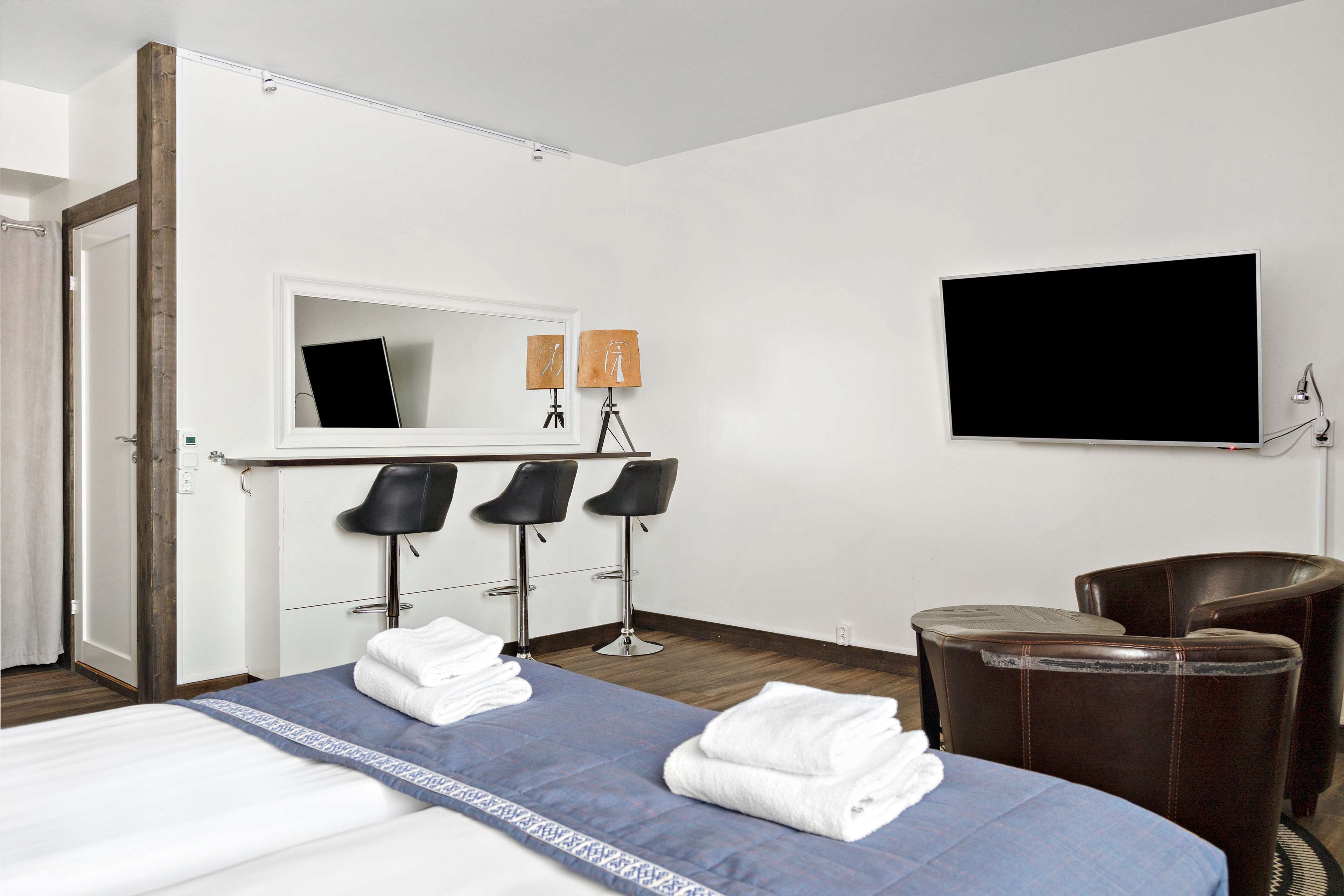 A hotel room with a bed, two chairs, a desk with a mirror, and a flat-screen TV.