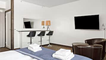 A hotel room with a bed, two chairs, a desk with a mirror, and a flat-screen TV.