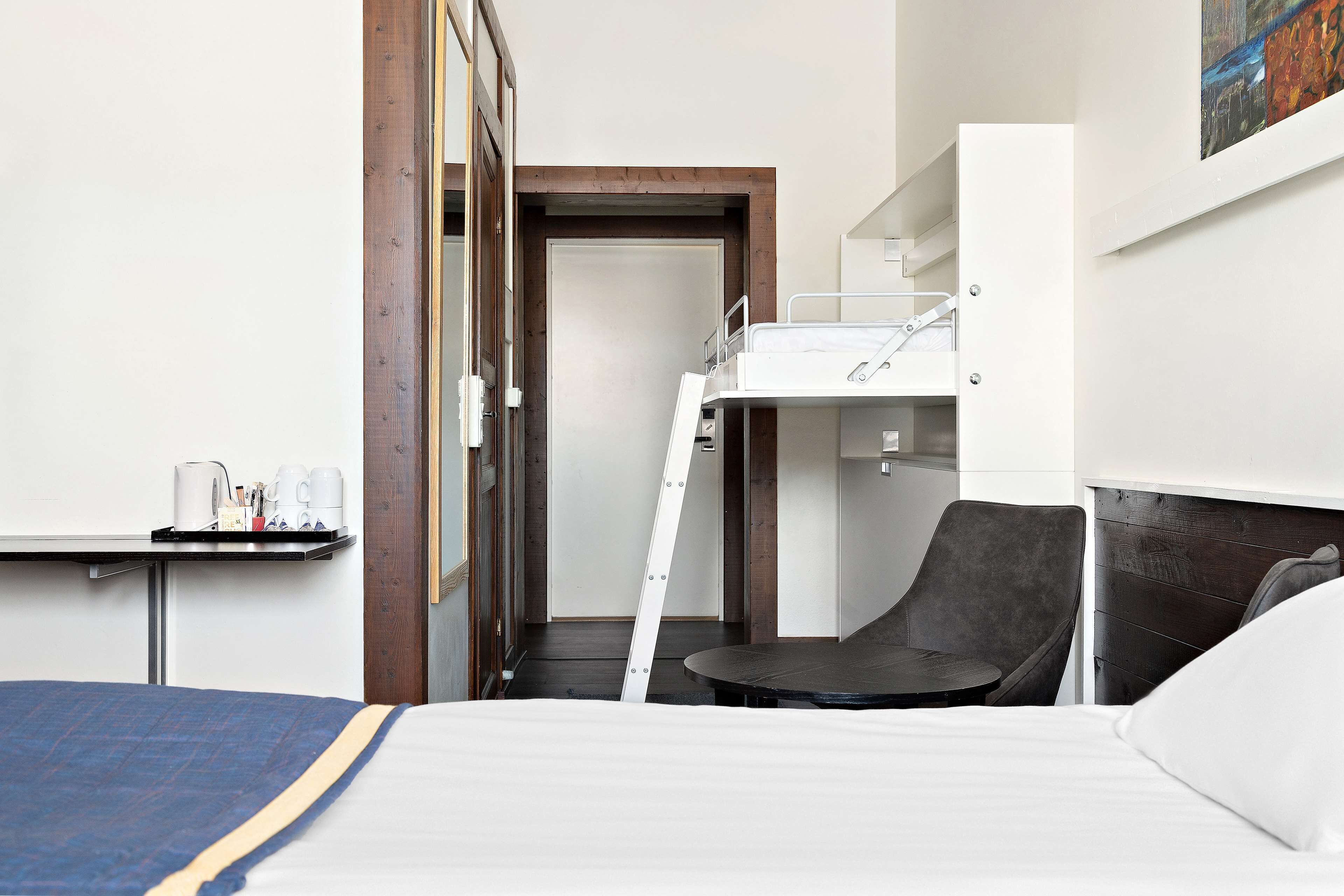 A hotel room with a bunk bed, a desk with a chair, and a small table with a tray of items.