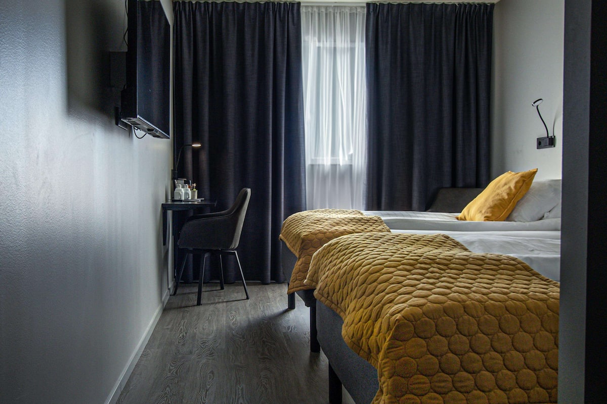 Ein Hotelzimmer mit zwei Betten, einem Schreibtisch, einem Stuhl und einem an der Wand befestigten Fernseher.