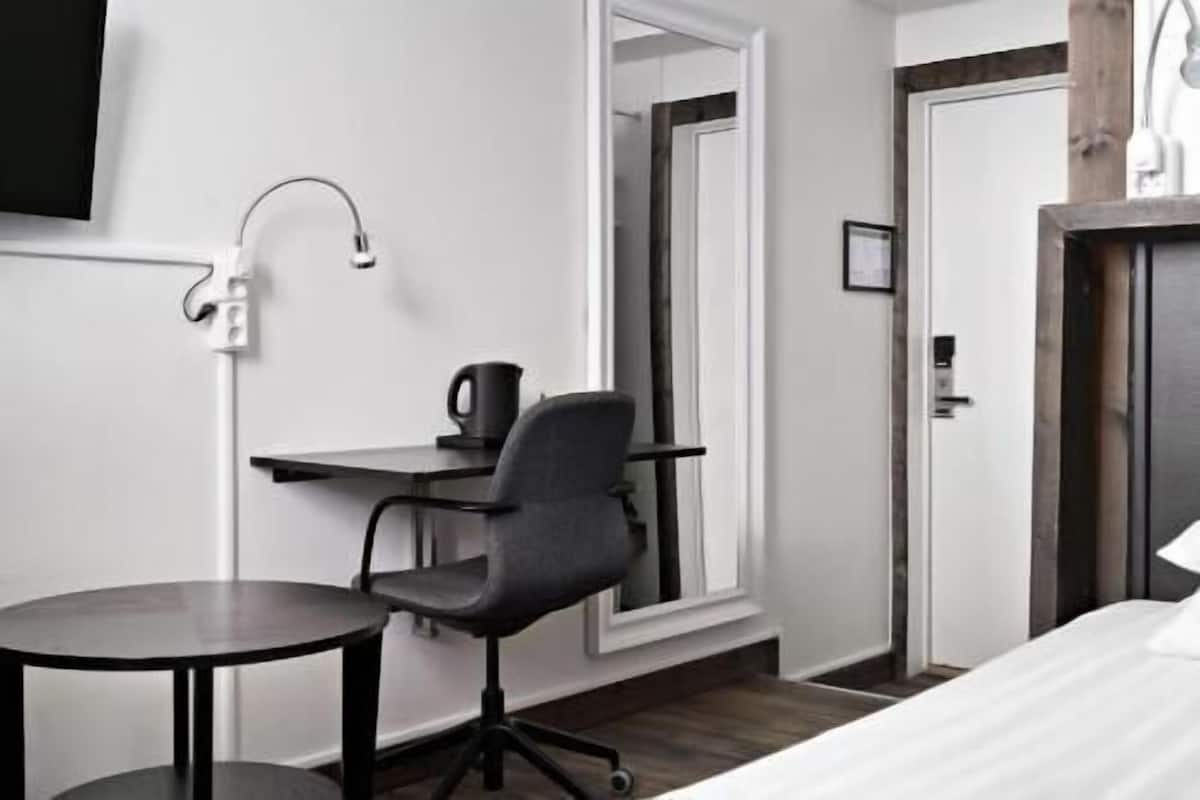 Ein Hotelzimmer mit Bett, Schreibtisch mit Stuhl, einem kleinen Tisch und einem Spiegel.