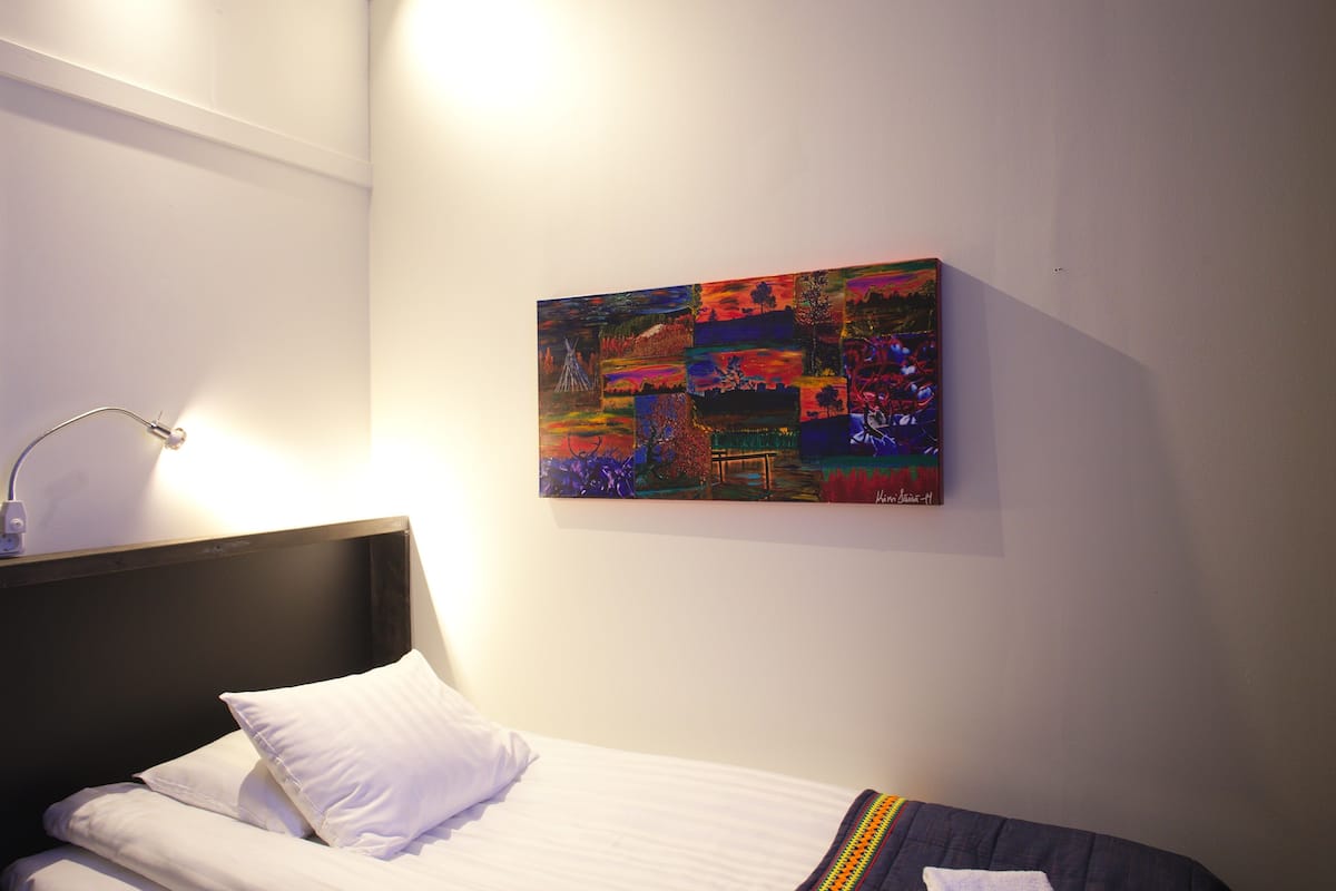 Ein ordentlich bezogenes Bett mit weißen Leinen und einem farbenfrohen abstrakten Gemälde darüber an der Wand.