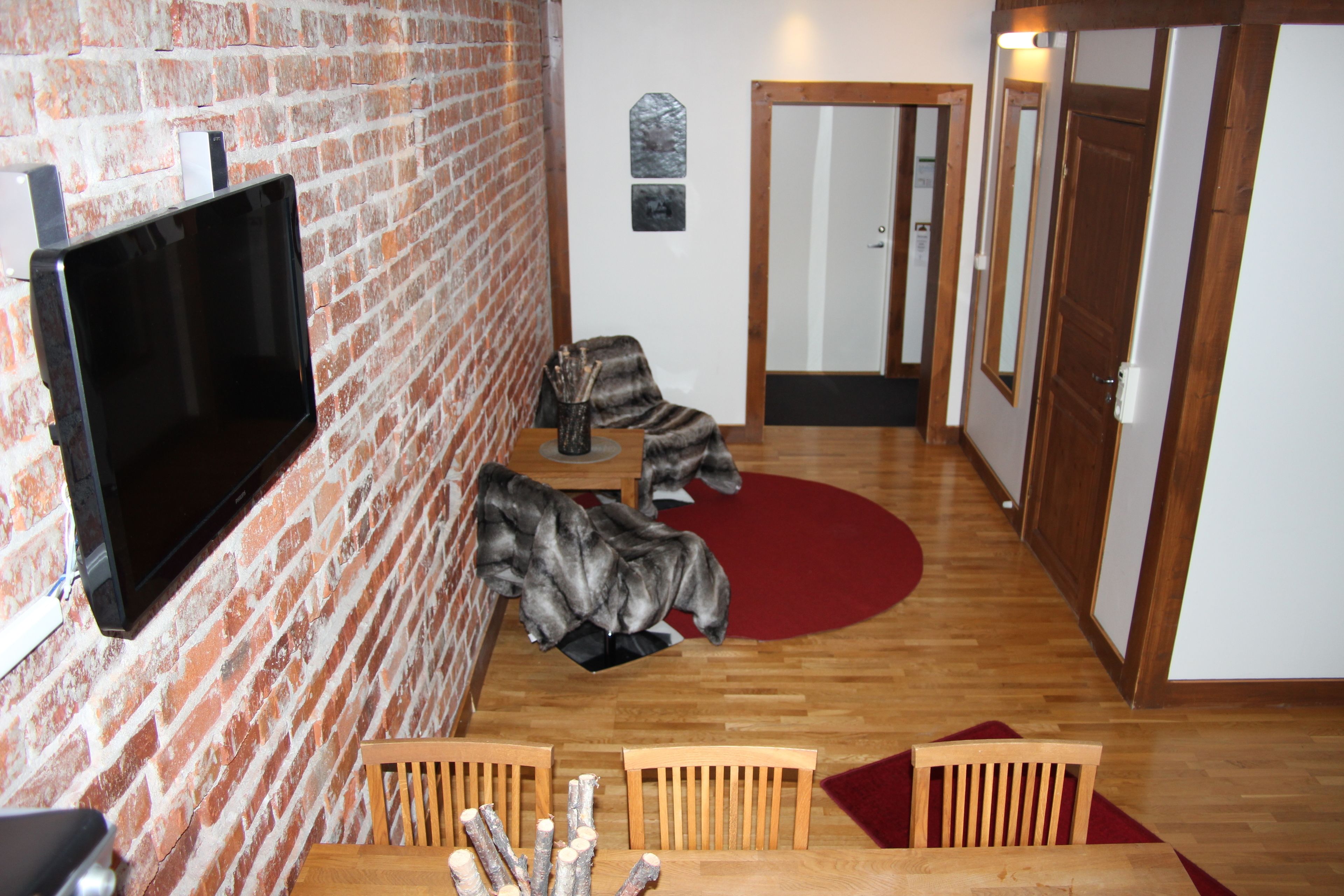 Ein Flur mit Backsteinwand, einem Wandfernseher, Holzstühlen und einem roten Teppich.