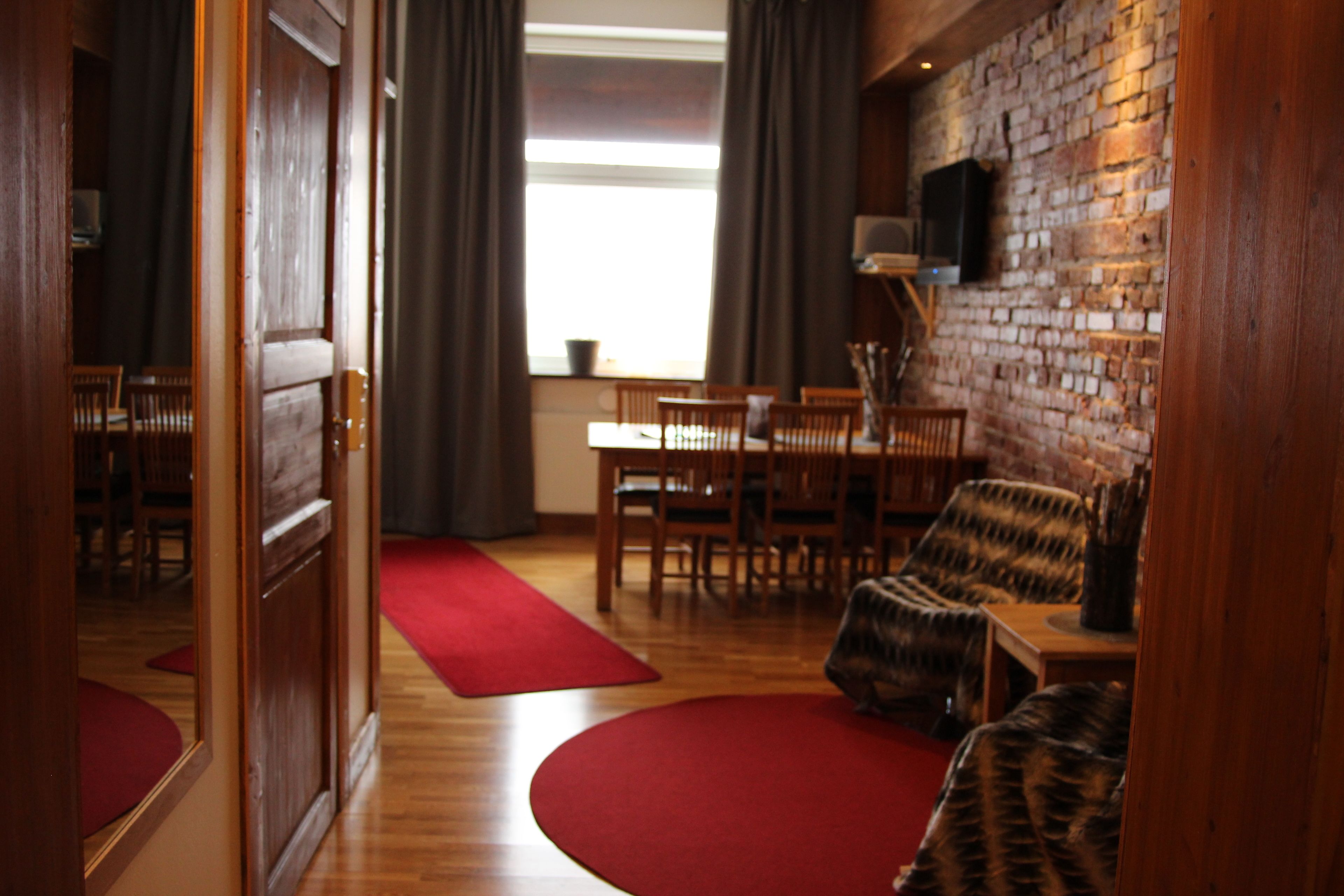Una habitación con pared de ladrillo, muebles de madera, alfombra roja y una ventana con cortinas.