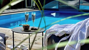 Área da piscina com espreguiçadeira, uma mesa pequena com petiscos e duas taças de champanhe, e um deck de madeira.