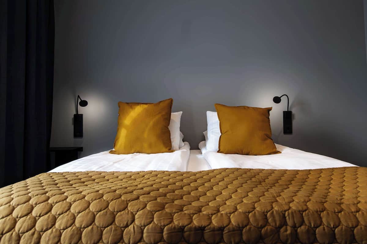 Ein ordentlich bezogenes Bett mit einer braunen gesteppten Tagesdecke, zwei Kissen und zwei Wandleuchten zum Lesen.