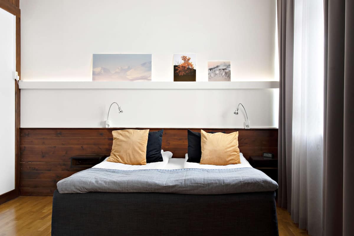 Ein modernes Schlafzimmer mit einem Holzkopfteil, einem großen Bett mit grauer Bettwäsche, zwei Nachttischen und drei gerahmten Bildern an der Wand.