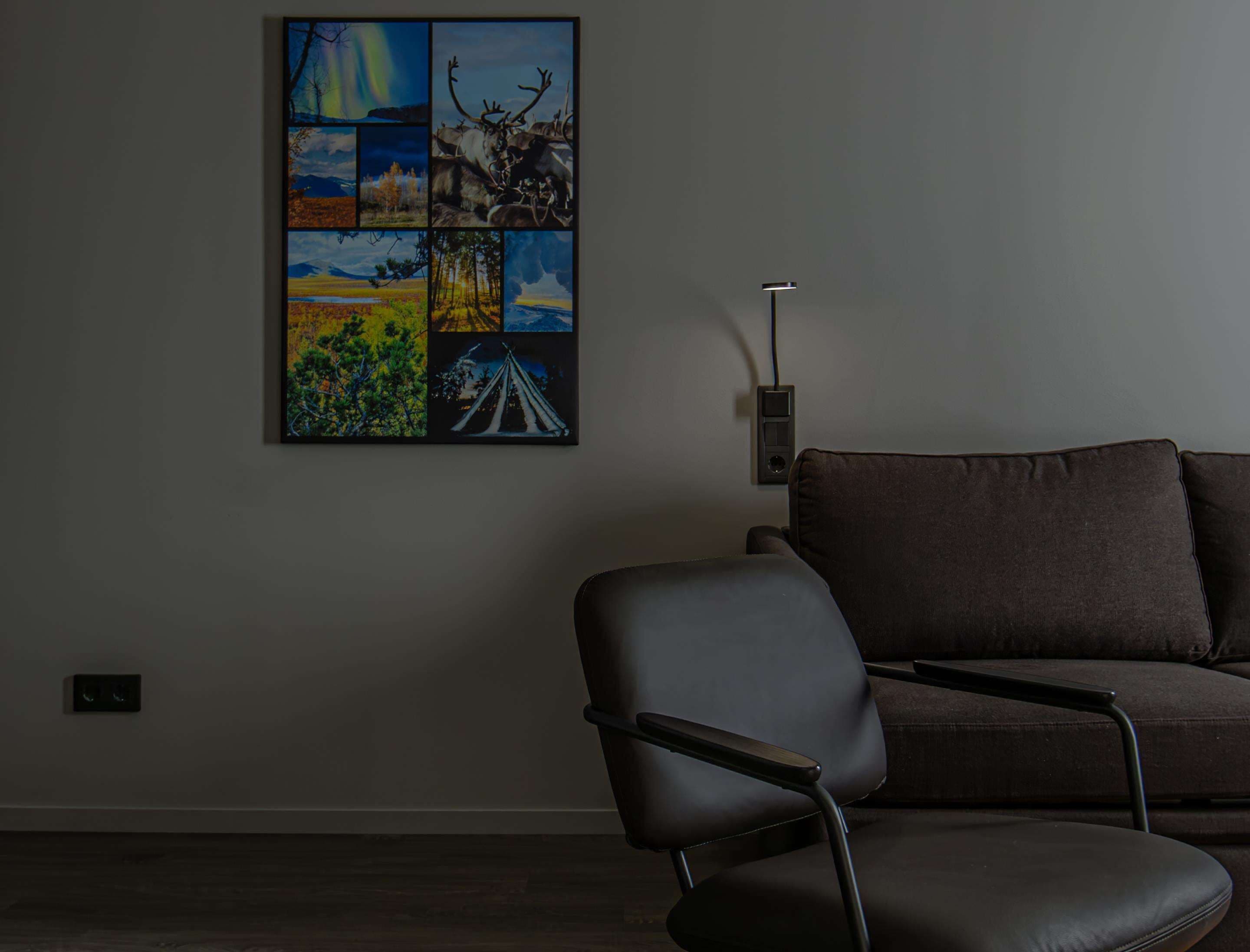 Una habitación con un sofá marrón oscuro y una silla negra. Se observa una toma de corriente fijada a la pared.