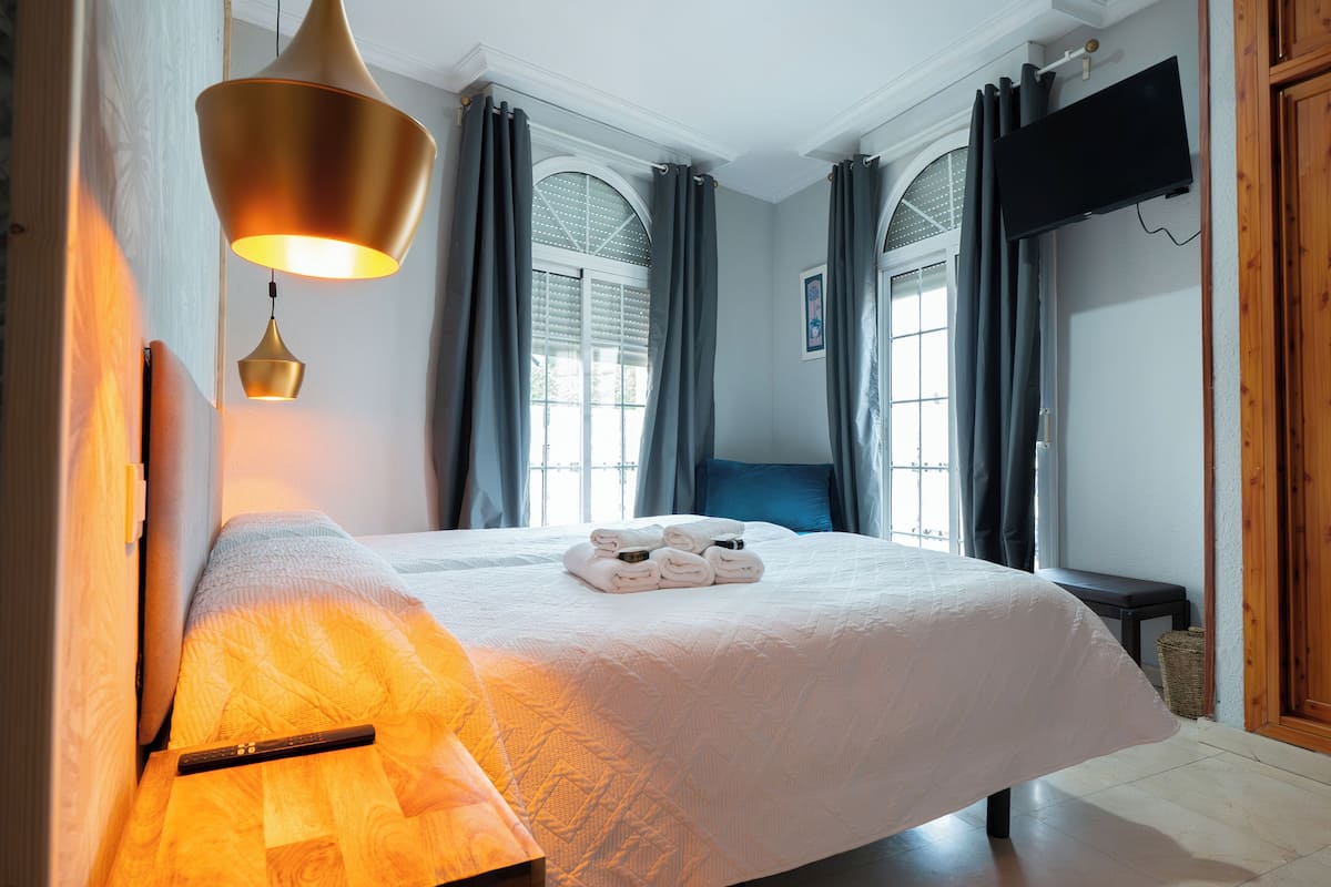 A hotel room with a large bed, a bedside lamp, a flat-screen TV, and a window with curtains.