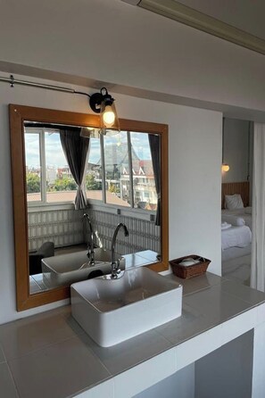 Um banheiro moderno com um espelho grande, uma pia branca e uma janela com cortinas.