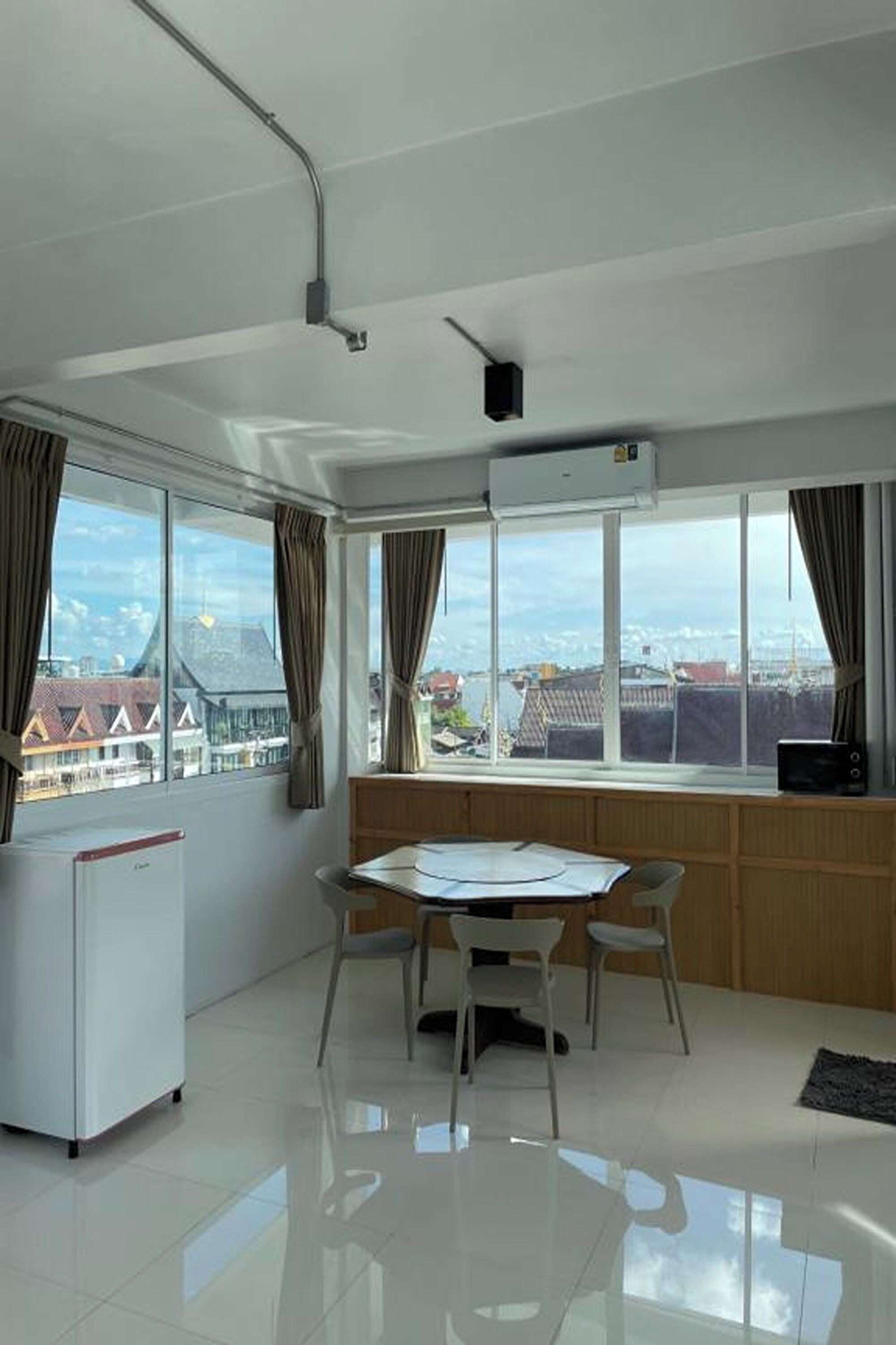 A modern room with a large window, a dining table, chairs, a small white cabinet, and a radiator.