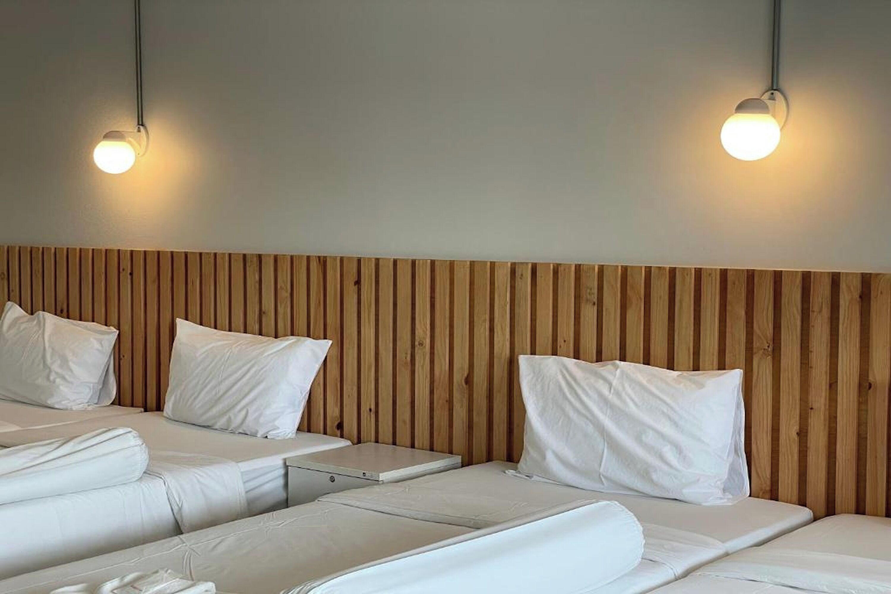 Habitación de hotel con dos camas, cabecero de madera e iluminación colgante.