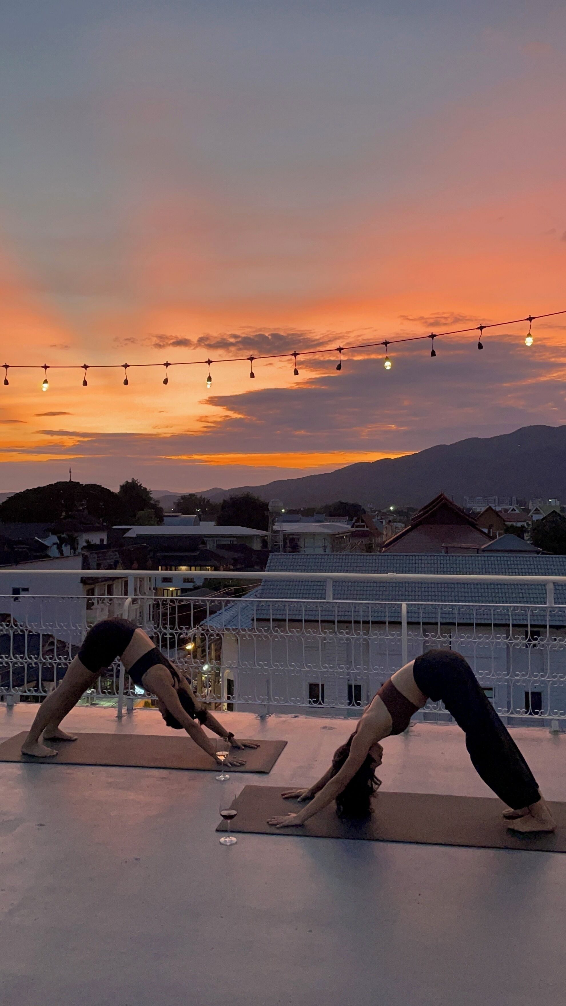 Two individuals performing yoga on outdoor mats with a cityscape and mountains in the background.