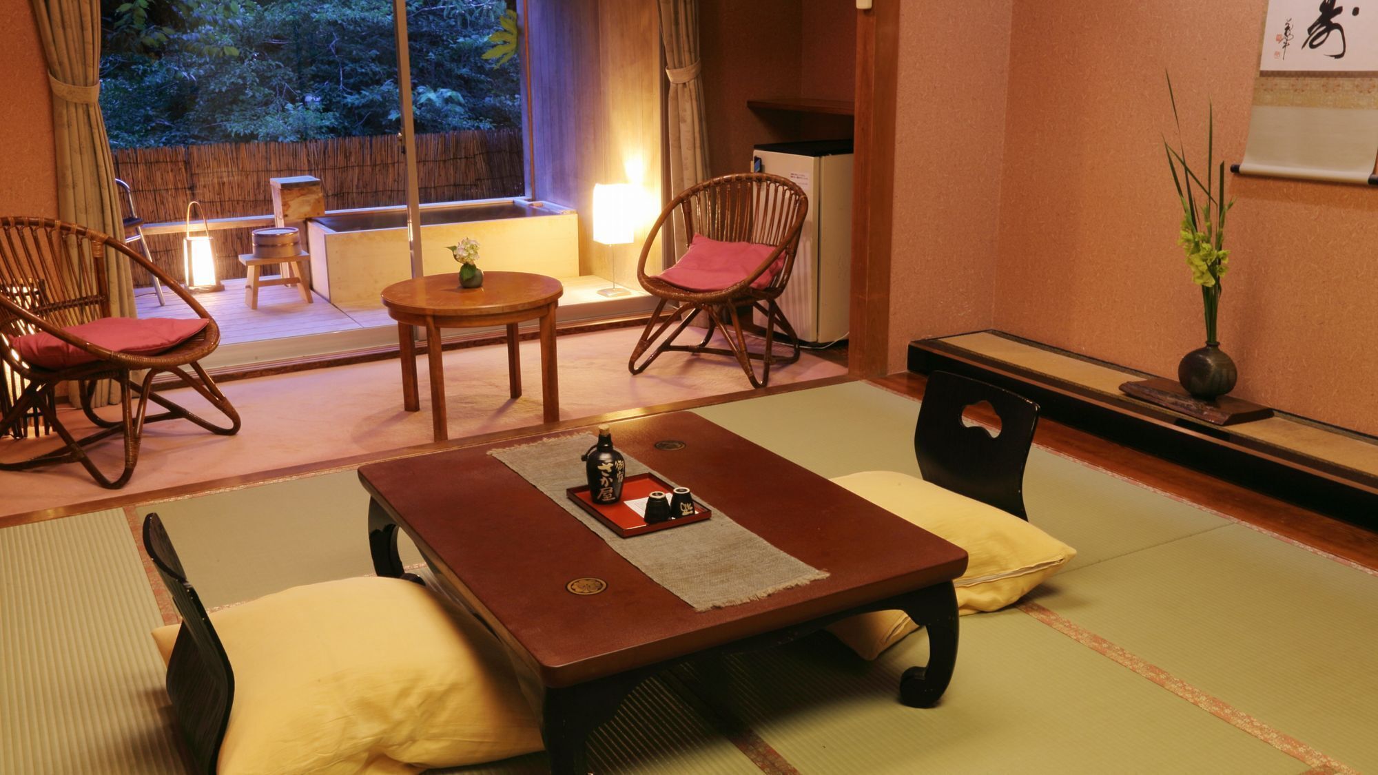 Una habitación japonesa tradicional con suelo de tatami, una mesa de madera baja y dos sillas de madera con cojines rojos.