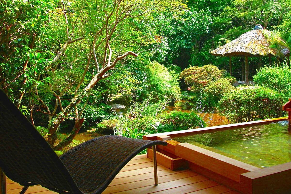 A wooden deck with a chair, a hot tub, and lush greenery.