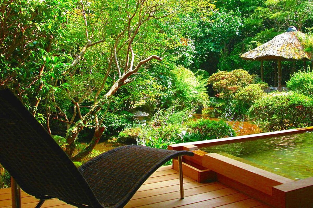 A wooden deck with a chair, a small pond, and a thatched-roof structure.